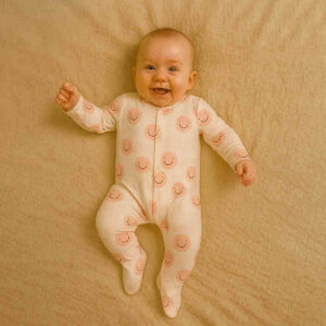 A toddler is wearing a Blush Smile Dreams Sleepsuit