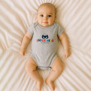 A toddler is wearing a future superhero baby bodysuit while lying on a soft cotton bedsheet