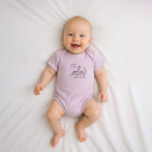 A toddler is wearing a little dino pals bodysuit