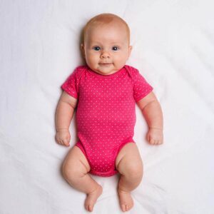 A toddler is wearing a pink sprinkle dots baby bodysuit