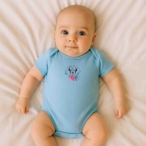 A toddler is wearing a sweet micky mouse printed baby bodysuit while lying down on a soft cotton bedsheet