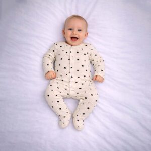 Baby geometric print sleepsuit with stars, moons, and shapes on a cream background