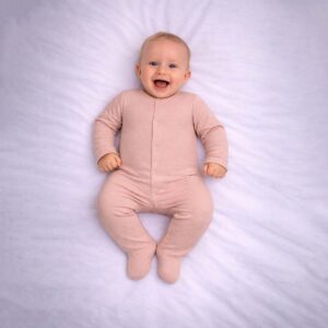 Peach polka dot baby sleepsuit worn by baby showing soft peach tone and white dots